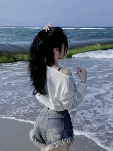 Sóng biển phía sau tôn dáng cô gái buộc tóc, áo trắng và quần short denim