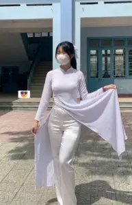 Sân nắng làm tà áo dài trắng bay nhẹ khi nàng đeo khẩu trang cầm vạt áo