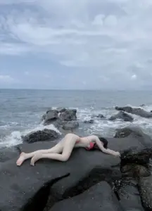 Giữa bãi đá ven biển xám, người đẹp nằm tạo dáng bên sóng xa trong không khí trầm