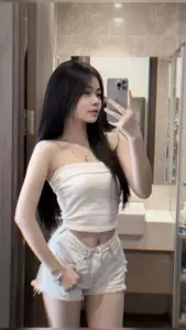 Selfie trong phòng thay đồ có cô gái áo trắng quần short, tóc dài và dáng đứng tự tin