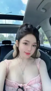 Trong xe hơi ánh sáng xanh, mỹ nhân mặc váy hồng cúi nhẹ với nụ cười tươi