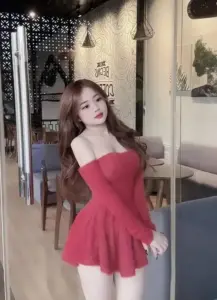 Tại góc quán ấm, cô gái váy đỏ trễ vai đứng nghiêng, môi hồng và tóc dài