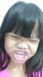 Cô bé tóc mái cười nhăn mặt, răng lộ rõ làm khoảnh khắc troll vui rất tự nhiên