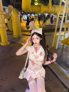 Dưới ánh đèn phố, gái đẹp váy hồng ngồi tạo dáng tinh nghịch bên cột vàng