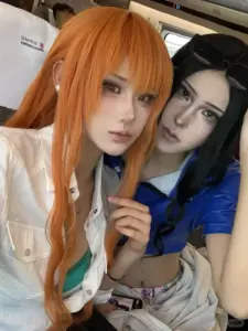 Coser nữ diện đồ Nami đứng cạnh mô hình tàu, tay cầm la bàn và nụ cười tươi rạng rỡ