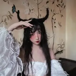 Trước tường hoa văn, cô nàng nâng tay tạo dáng, váy trắng nổi bật cùng sừng đen