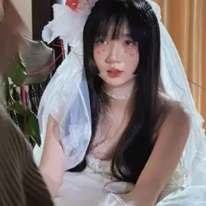 Gần khung cửa gỗ, cô gái đội voan trắng, tóc đen phủ vai, trang điểm nhẹ
