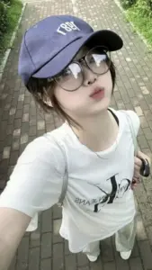 Từ góc cao, nàng đội mũ lưỡi trai và đeo kính nhìn máy thật đáng yêu