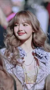 Lalisa Manobal mỉm cười ngọt ngào, tóc nâu bồng bềnh nổi bật trên nền sân khấu mờ