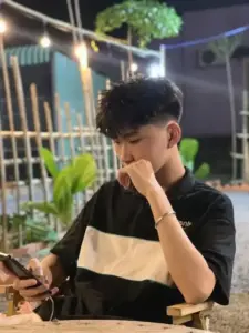 Khoảnh khắc ngồi quán ngoài trời, áo polo đen be và dáng nhìn điện thoại tập trung