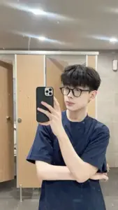 Selfie trước gương trong phòng sáng, áo thun đen và kính mắt tạo vẻ tri thức