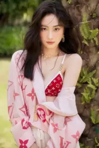 Gương mặt nàng thơ trong áo khoác hồng nổi bật giữa nền cây xanh, mái tóc xoăn mềm