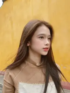 Nền vàng ấm làm cô gái nghiêng mặt thanh lịch, tóc nâu dài ôm nhẹ bờ vai