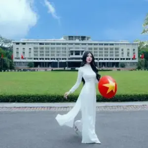 Sân trường rộng phía sau cô gái mặc áo dài trắng, tay cầm cờ đỏ sao vàng