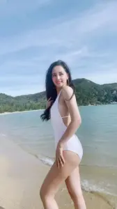 Ở mép sóng, Mai Phương Thúy diện áo tắm trắng cười nhẹ, tóc dài bay tự nhiên
