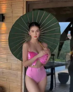 Bàn tay cầm ô xanh làm nổi bộ bikini hồng và gương mặt trang điểm sắc