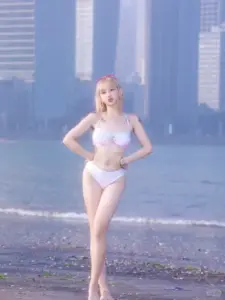 Từ xa, cô gái tóc vàng diện bikini trắng tạo dáng thẳng giữa bãi biển và cao ốc