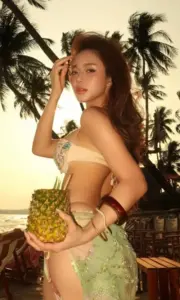 Ánh nắng chiều phủ lên cô nàng bikini vàng cầm dứa, tóc nâu xoăn bên hàng dừa