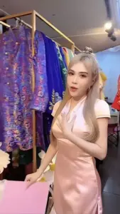 Gần khu váy áo lấp lánh, Thân Thùy Bảo Trân mặc đồ hồng satin, ôm ly nhìn thẳng