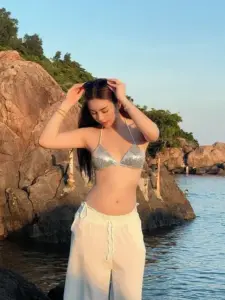 Dáng đứng bên vách đá, cô gái bikini xám kéo nhẹ tóc, quần trắng bay trong nắng