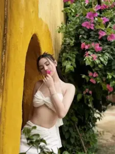 Tựa tường vàng cạnh hoa giấy, cô gái bikini kem chạm môi, mắt nhìn mơ màng