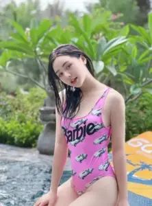 Trong bộ đồ bơi hồng, cô gái tóc ướt ngồi cạnh hồ, mỉm cười bên cây xanh