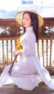 Cô gái áo dài trắng đội nón ngồi bên lan can, pose áo dài mềm giữa nắng sáng