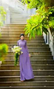 Người đẹp áo dài tím đứng trên bậc thang xanh, tay cầm hoa và dáng người thanh thoát