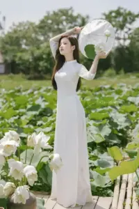 Cô gái áo dài trắng tạo dáng giữa đầm sen, tay nâng nón và gương mặt nghiêng mềm