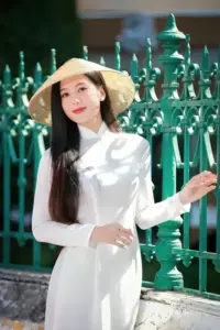Thiếu nữ áo dài trắng đứng bên hàng rào xanh, nét duyên Việt hiện rõ trong ánh mắt