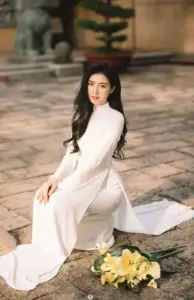 Cô gái áo dài kem ngồi trên nền đá cổ, tà áo trải nhẹ và gương mặt điềm tĩnh