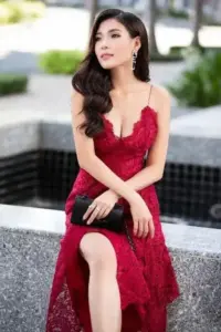 Trong váy đỏ ren, cô gái ngồi nghiêng bên hồ, gương mặt dịu dàng và tóc xoăn mềm