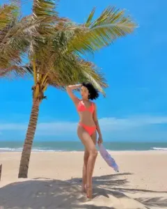 Khung biển rộng ôm lấy dáng người đẹp mặc bikini đỏ cam, tay vuốt tóc tự nhiên