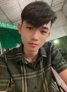 Bạn nam mặc sơ mi caro ngồi trong lớp, tóc mái gọn và nụ cười nhẹ rất tự nhiên