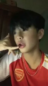 Bạn nam mặc áo bóng đá đỏ tạo dáng trong ánh sáng mờ, tóc mái rối nhẹ và biểu cảm vui