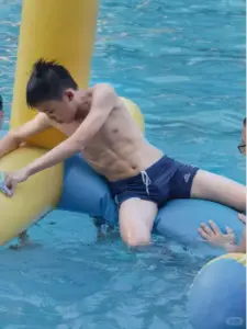 Bên hồ bơi, trai K9 ngồi trên phao xanh, tóc ướt và dáng vẻ năng động