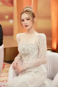 Trong bộ váy cưới trắng ôm dáng, cô gái tóc vàng ngồi nghiêng nhẹ với vẻ ngoài sang trọng